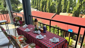 A terrace with a table set for tea, chairs, and a view of trees and buildings. - Kilimanjaro Smiley Inn (Moshi)