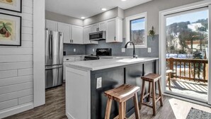 Una cocina moderna con armarios blancos, electrodomésticos de acero inoxidable, una isla grande con taburetes y vistas a un paisaje nevado a través de un ventanal.