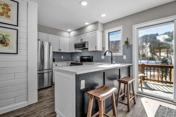 Una cocina moderna con armarios blancos, electrodomésticos de acero inoxidable, una isla grande con taburetes y vistas a un paisaje nevado a través de un ventanal.