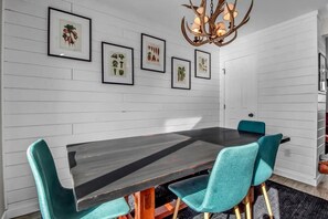Uma sala de jantar com uma mesa de madeira escura, cadeiras verde-água e gravuras botânicas emolduradas na parede.