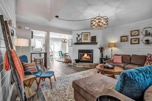 A living room with a fireplace, a dining area, and a kitchen visible through an open door. - Modern Townhome, 2 Decks, Fireplace (Ellicottville)