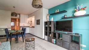 A modern living room with a teal accent wall, a flat-screen TV, and a dining area with blue chairs. - Cozy apartment in Oostende with WiFi (Oostende)