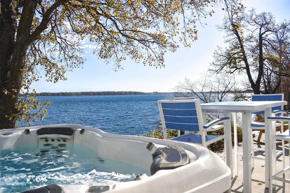 A hot tub with a view of a lake, surrounded by chairs and a table.