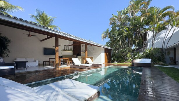 A poolside area with lounge chairs, a wooden deck, and a covered seating area with a ceiling fan.