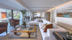 A modern living room with a white sofa, a coffee table, and a dining area in the background.