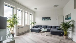 Ein modernes Wohnzimmer mit einem grauen Ecksofa, einem Glastisch und zwei Blumentöpfen.