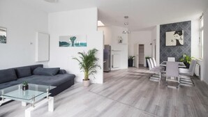 Ein modernes Wohnzimmer mit grauem Sofa, einem Glastisch und einem Essbereich mit weißem Tisch und Stühlen.