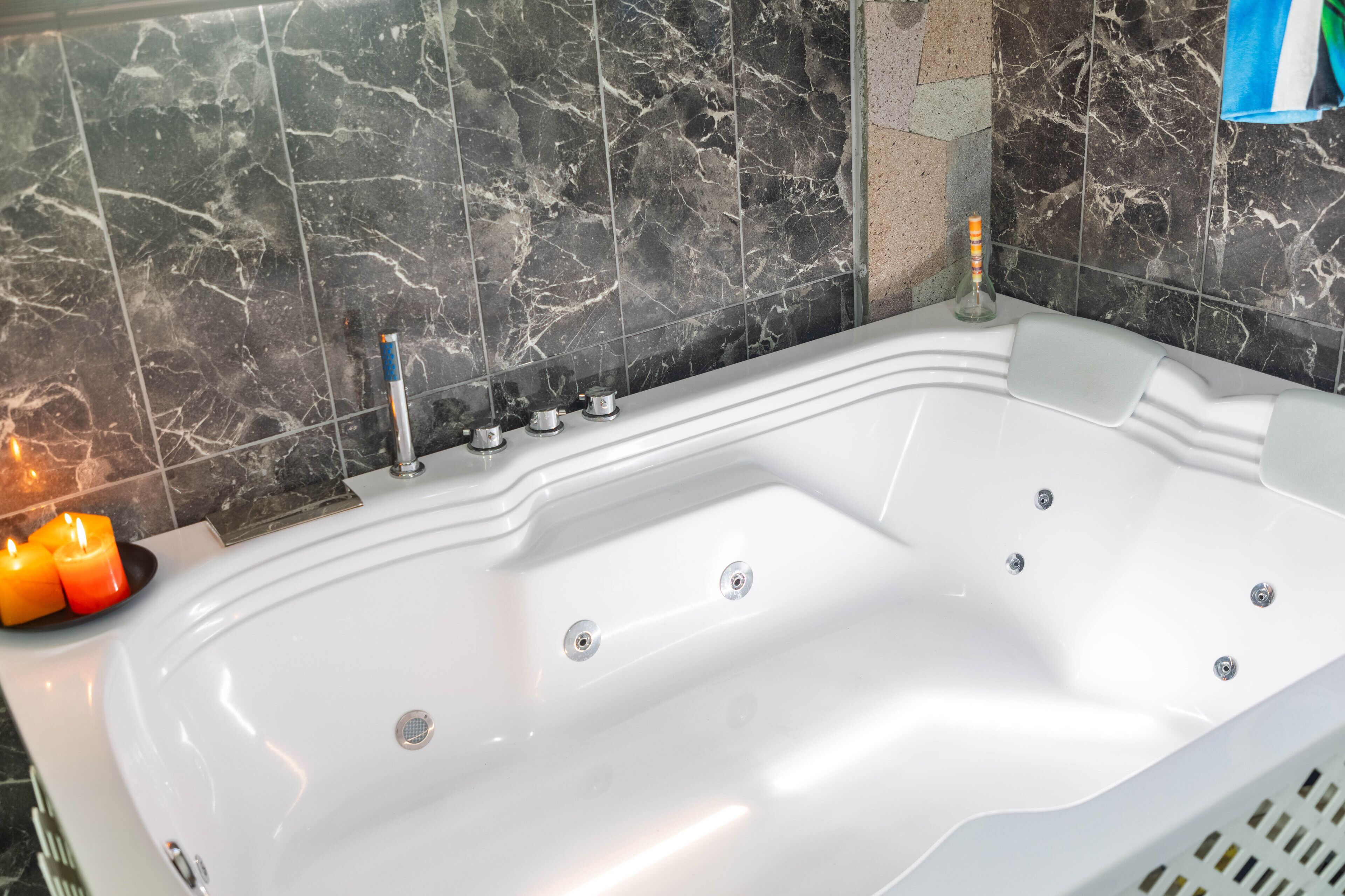 A modern bathroom with a white bathtub, marble tiles, and a row of candles.