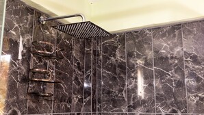 Ein Badezimmer mit schwarzem Marmor an der Wand, einer Dusche inklusive schwarzem Duschkopf im Regenstrahlmodell und einem Metallhandtuchhalter.