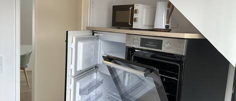 A compact kitchen with a built-in oven and microwave, a wooden countertop, and a door leading to a dining area.