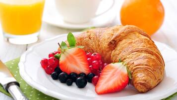 Une assiette de petit-déjeuner comprenant un croissant, des fraises, des groseilles rouges et des myrtilles, un verre de jus d’orange et une tasse de café.
