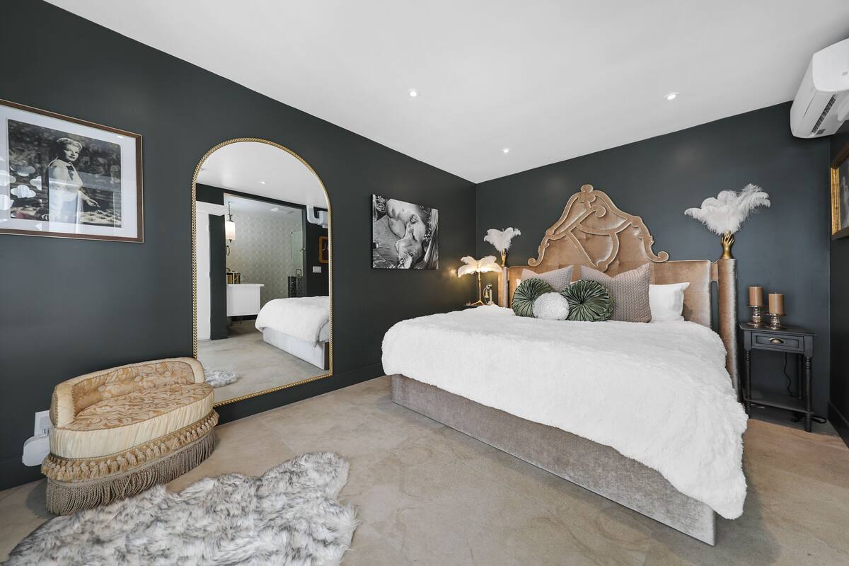 A modern bedroom with a large bed, a mirror, and a decorative headboard.