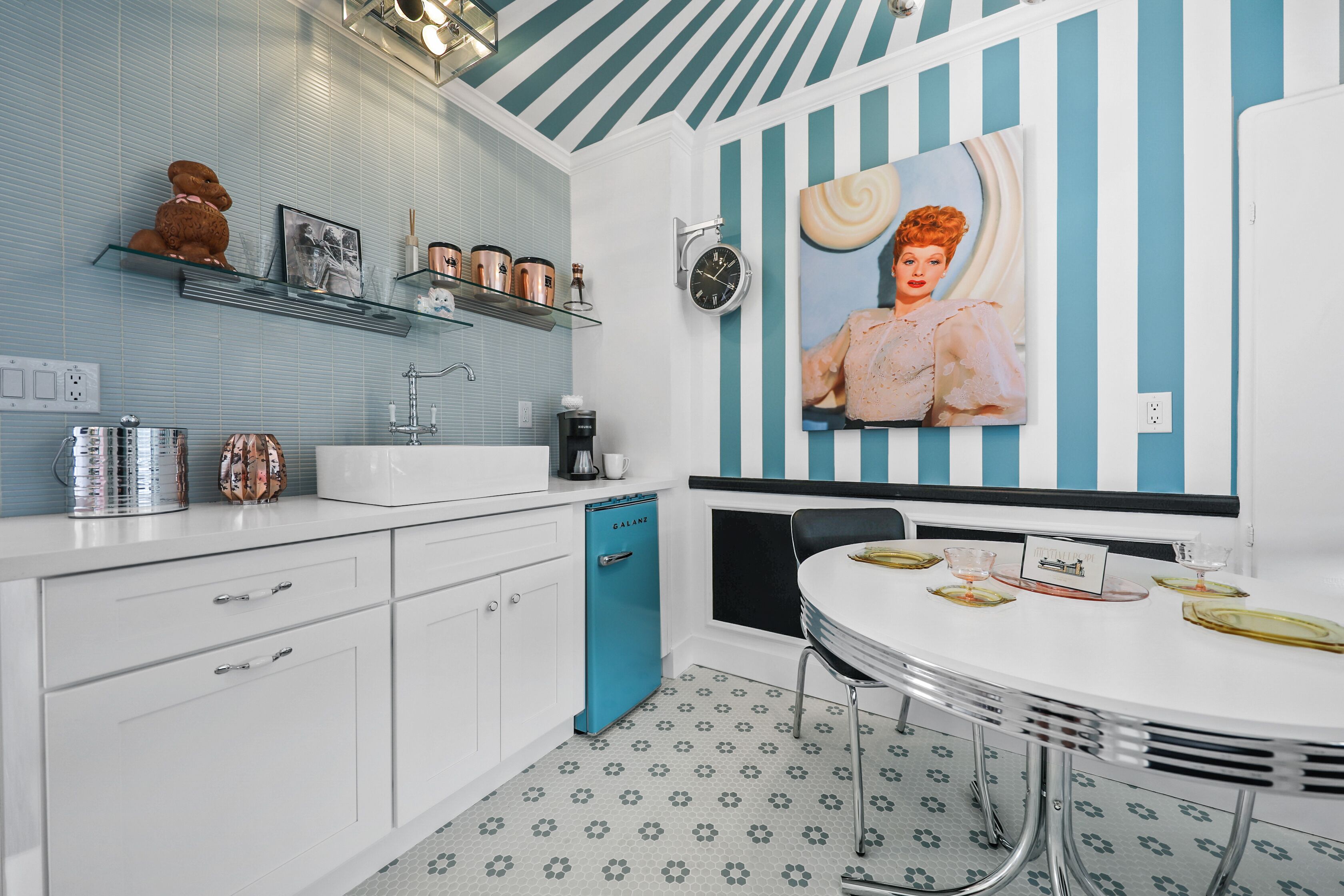 A modern kitchen with white cabinets, a blue dishwasher, and a dining area with a round table and chairs.