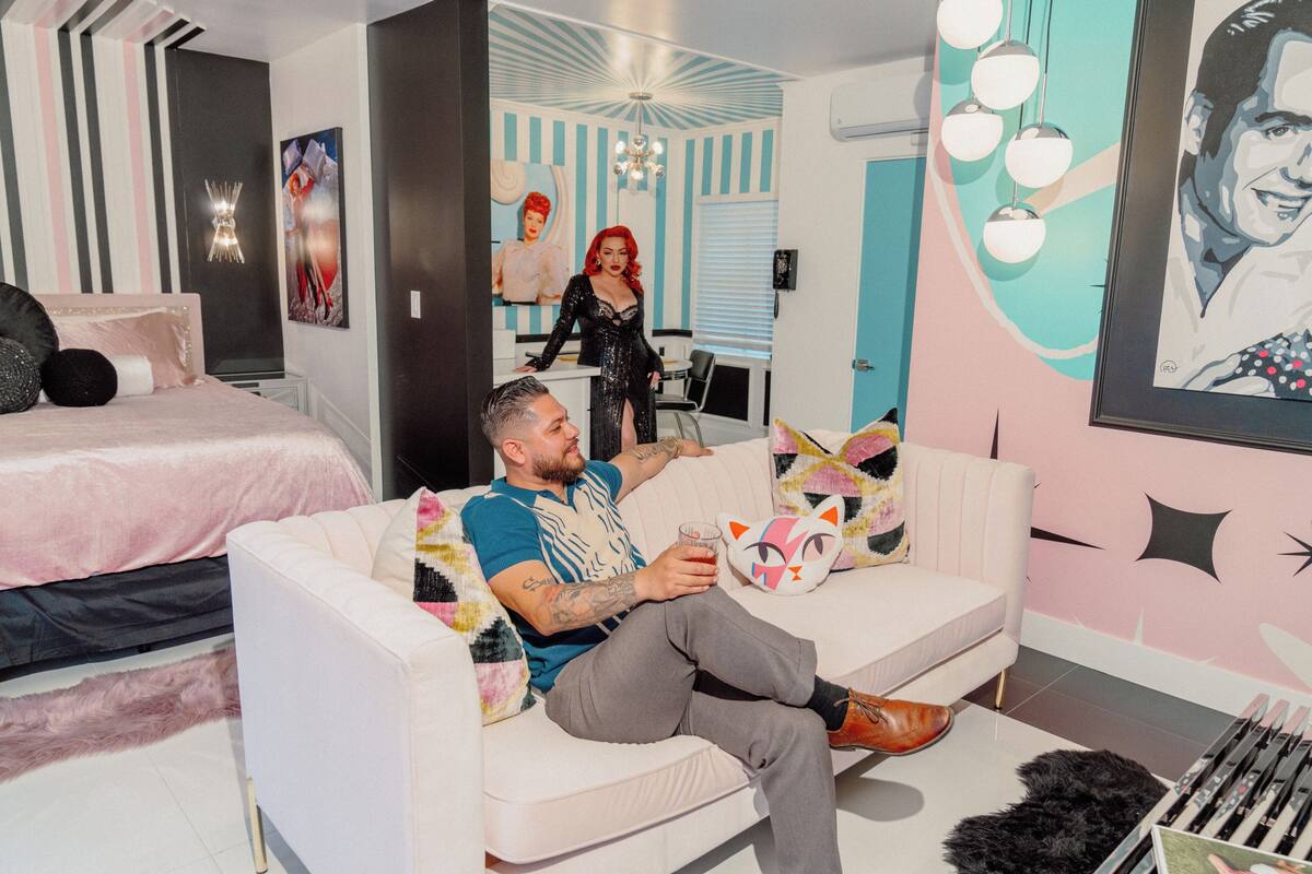 A modern living room with a white sofa, a bed with a pink bedspread, and a cat-shaped pillow.