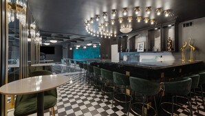 Un espace bar avec un sol à carreaux, des tabourets de bar verts et un lustre moderne.