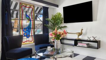 A modern living room with a glass coffee table, a blue sofa, a decorative vase with flowers, and a mounted TV.