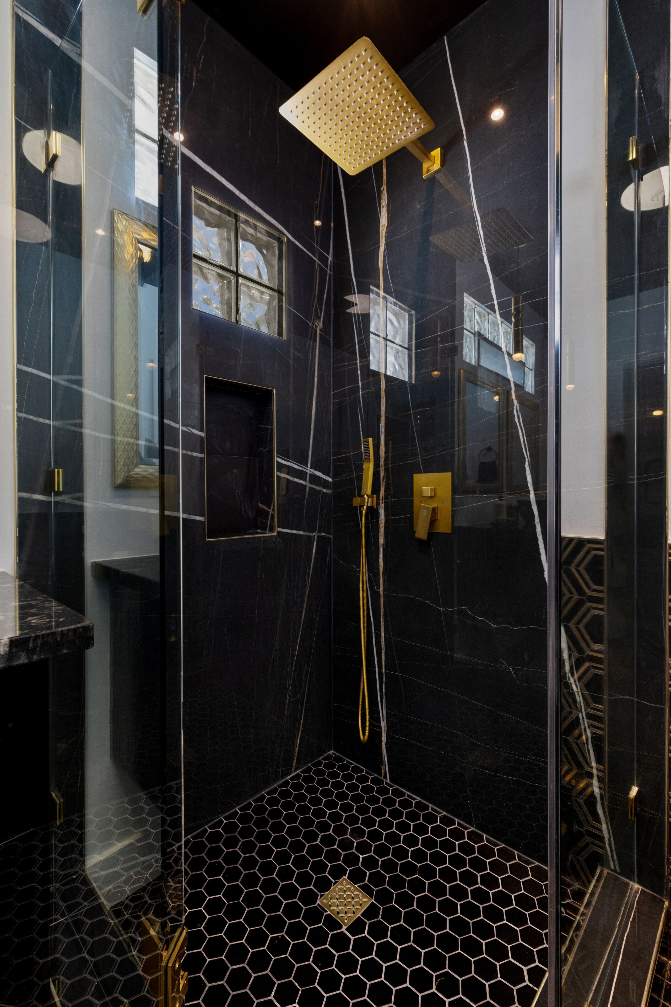 A modern shower with a geometric floor pattern, a glass enclosure, and a gold showerhead.