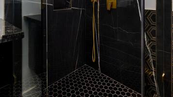 A modern shower with a geometric floor pattern, a glass enclosure, and a gold showerhead.