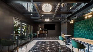 Un intérieur moderne avec un piano, des fauteuils à revêtement vert et un sol orné de motifs géométriques.