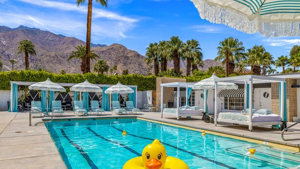 Une piscine avec un canard gonflable jaune, des chaises longues et une vue sur les montagnes.