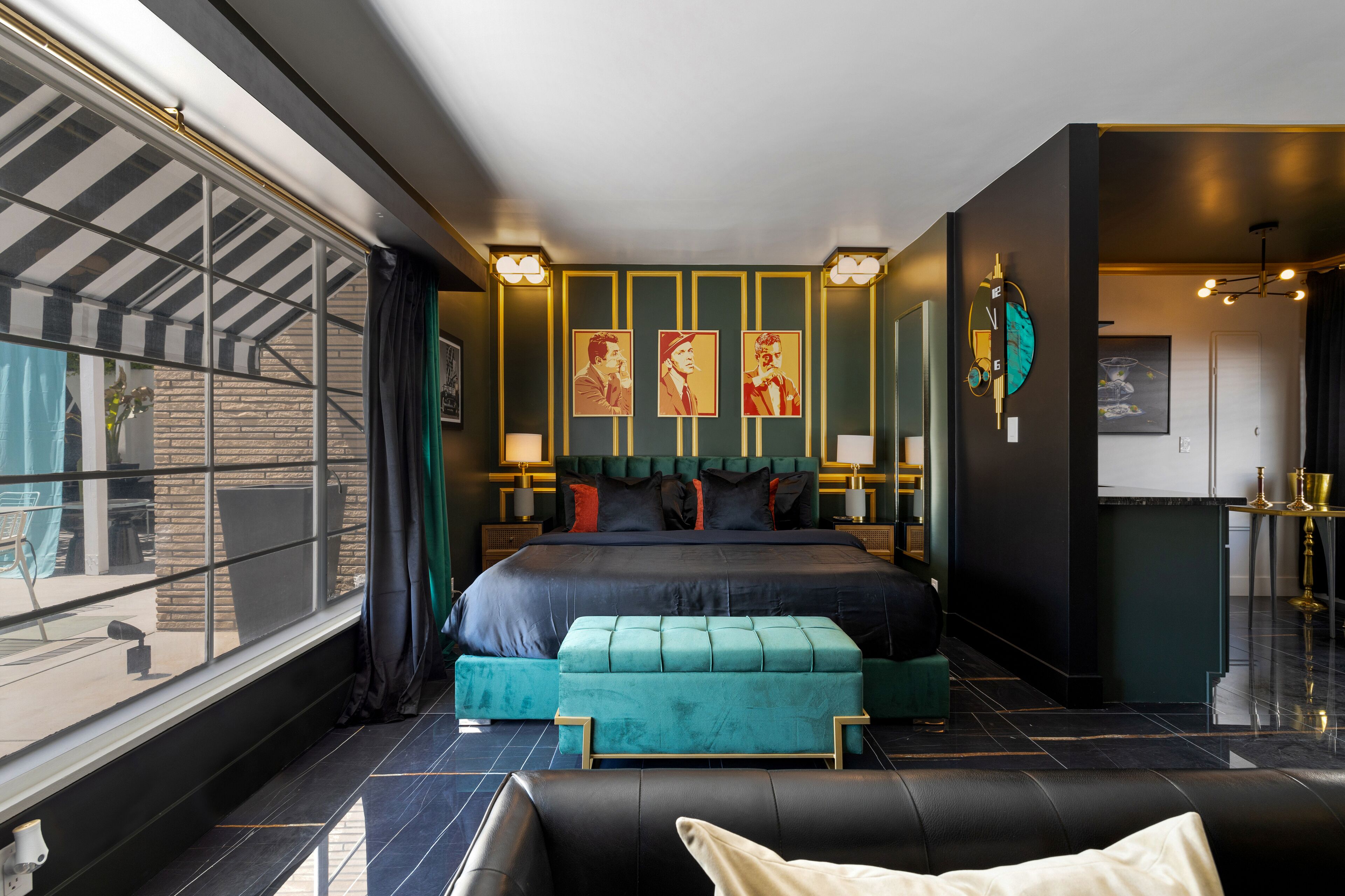 Ein modernes Schlafzimmer mit einem großen Bett, einem türkisfarbenen Hocker und Blick ins Freie durch ein großes Fenster.