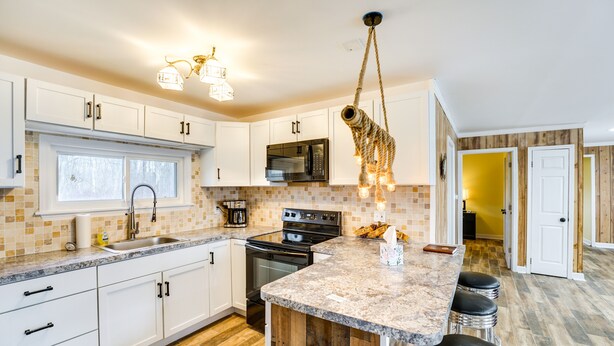 A modern kitchen with white cabinets, a granite countertop, a hanging light fixture, and a wooden island with bar stools. - Quiet Country Home By Shay Lake! (Silverwood)