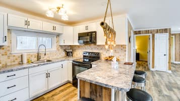 A modern kitchen with white cabinets, a granite countertop, a hanging light fixture, and a wooden island with bar stools.