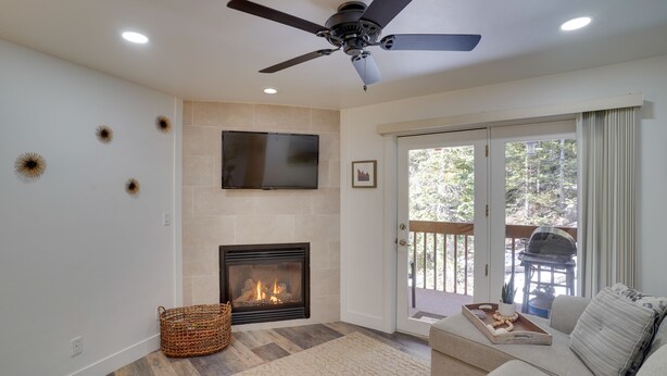 A living room with a fireplace, a ceiling fan, a flat-screen TV, and a sliding glass door leading to an outdoor area. - Brian Head Condo w/ Balcony, Grill & Mountain View (Brian Head)