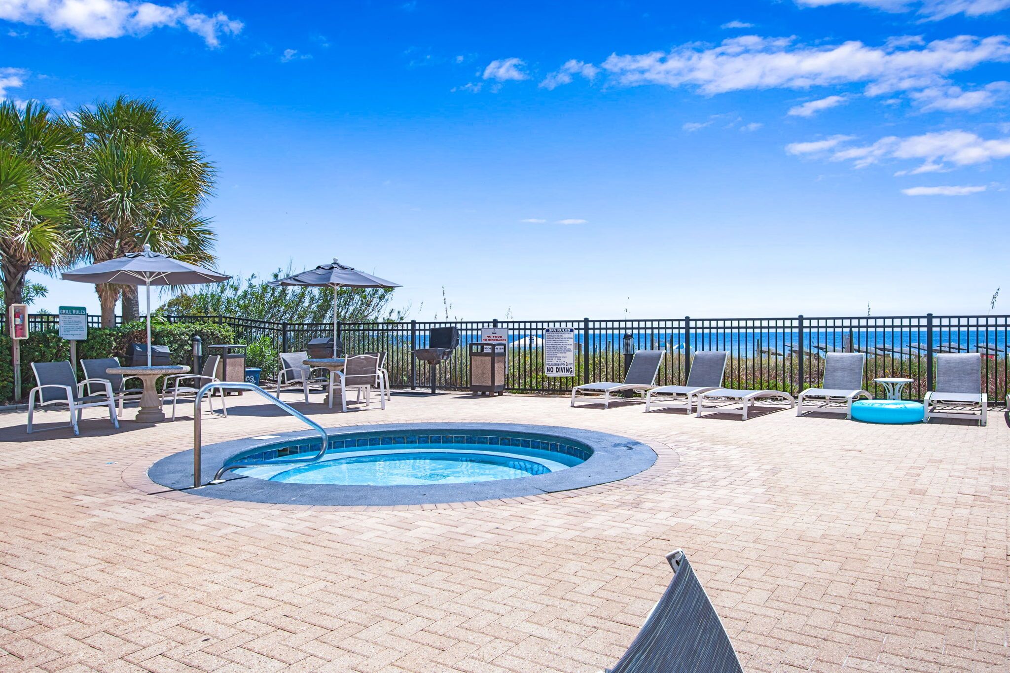 Uma área de piscina com espreguiçadeiras, uma banheira de hidromassagem e vista para o oceano.