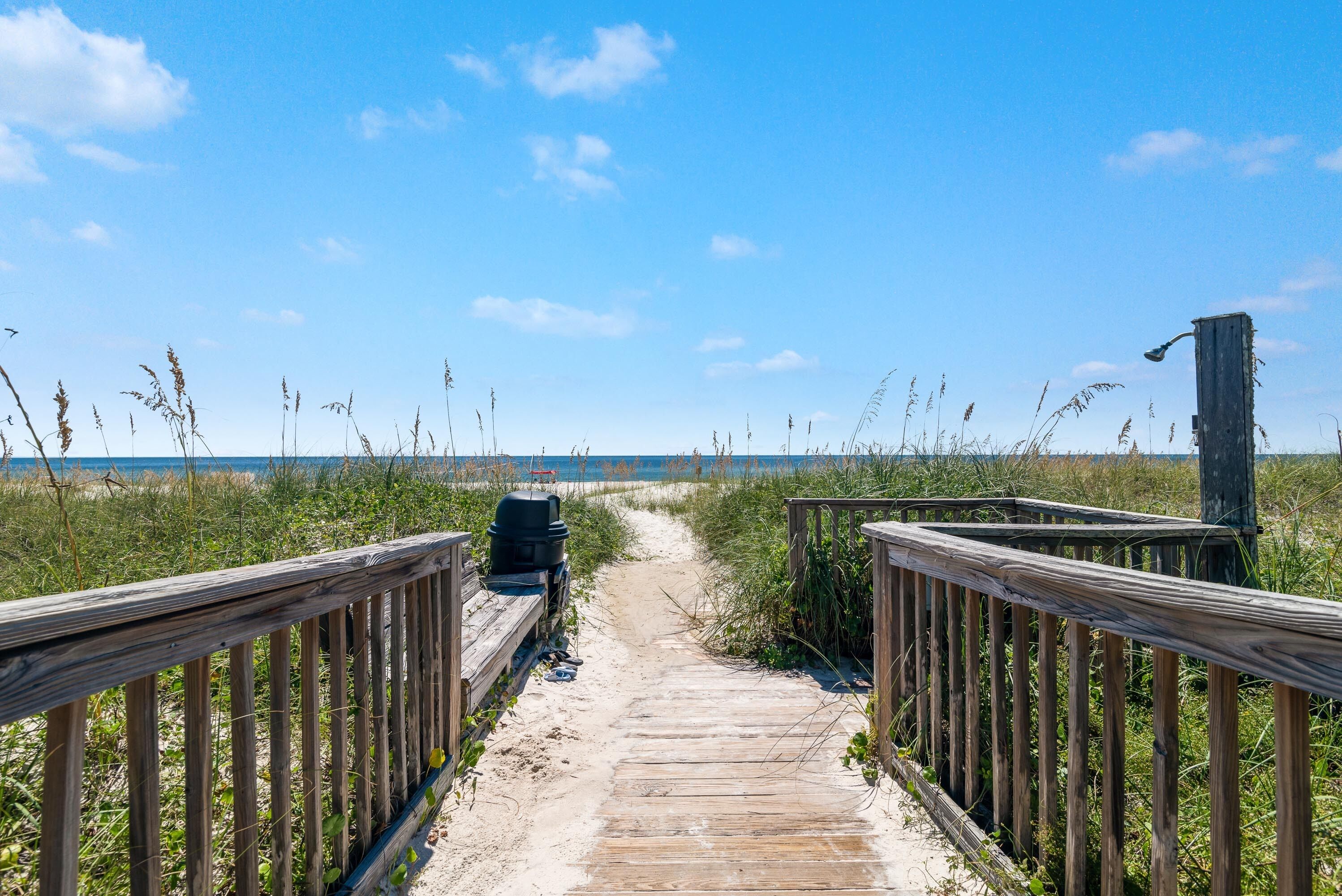 A wooden boardwalk leading to a beach with a wooden structure on the right.