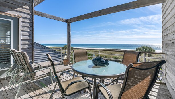 Un espacio de estar al aire libre cubierto con una mesa y sillas de vidrio, con vistas a una playa.