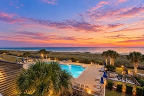 A pool area with lounge chairs and umbrellas, overlooking a beach and ocean at sunset. - Needle Rush Point B32 | Walk to Florabama | Riverside & Beachside Pools | My Beach Getaways (Pensacola)
