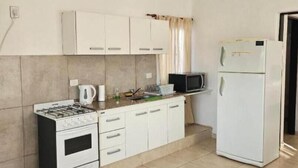 A compact kitchen with white cabinets, a gas stove, a microwave, and a refrigerator.