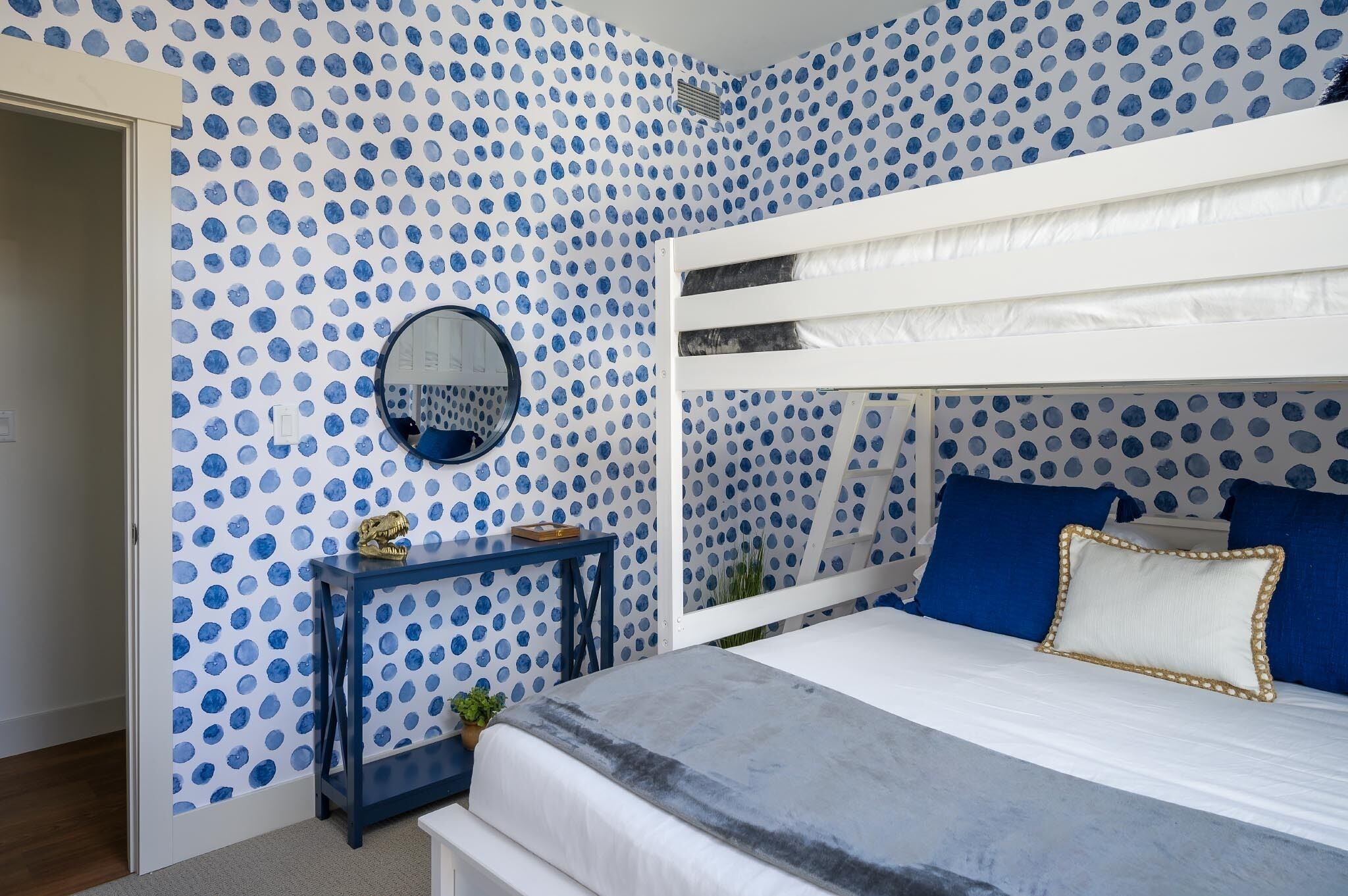 A bedroom with a bunk bed, a round mirror, a small table, and a polka dot wallpaper.