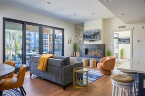 A modern living room with a grey sofa, a round glass table, and a fireplace.