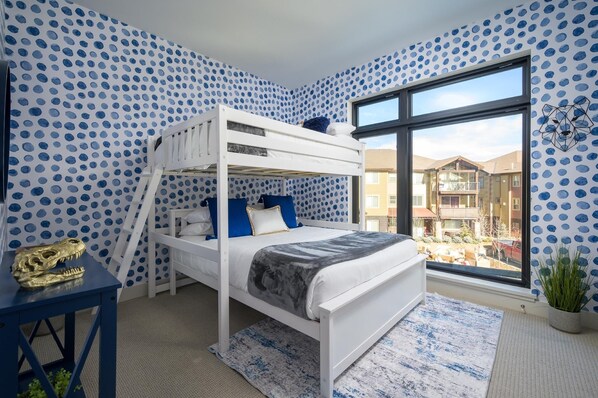 A bunk bed room with polka dot wallpaper, a large window, and a view of buildings outside.