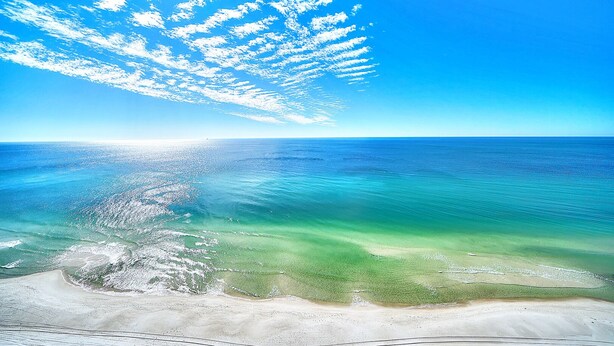 Una playa con aguas turquesas cristalinas, una orilla arenosa y un cielo azul brillante con nubes dispersas.