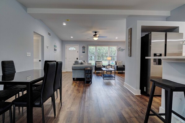 A modern living room with a dining area, a kitchen, and a ceiling fan.