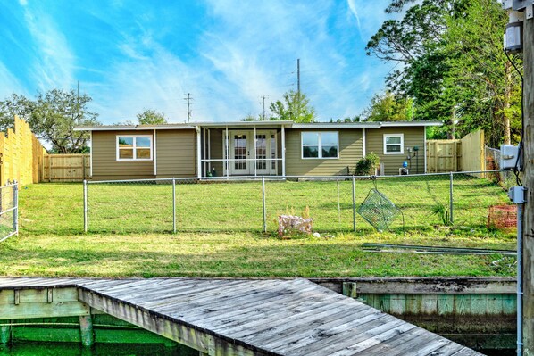 A single-story house with a fenced yard, a wooden dock, and a grassy area. - BayFront Home with Boat Dock (Panama City Beach)