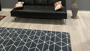 Ein modernes Wohnzimmer mit einer schwarzen Couch, einem Teppich mit geometrischem Muster und einer Wanduhr.