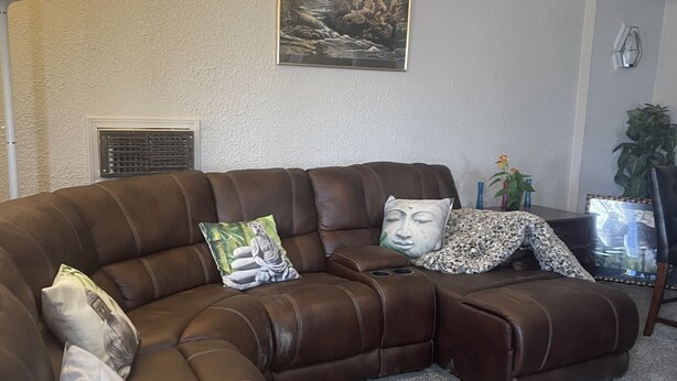 Un sofá seccional de cuero marrón con almohadones decorativos, una obra de arte enmarcada en la pared y una pequeña mesa con un taladro.