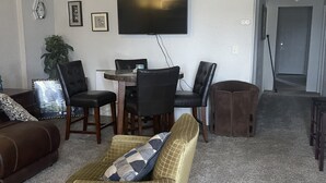 Una sala de estar con un sofá, sillas, una mesa de centro, un televisor y una planta.