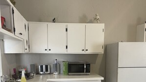 Una cocina con armarios blancos, un microondas, un refrigerador y una encimera con varios objetos.