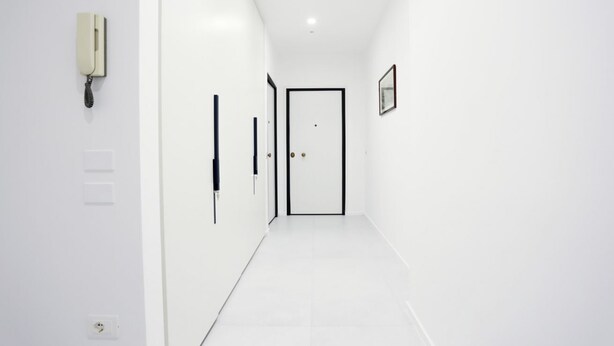 Un pasillo estrecho con una pared blanca, una puerta al final y un teléfono fijo en la pared.