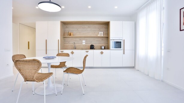 A modern kitchen with white cabinets, a built-in oven, and a dining area with wicker chairs and a white table. - GuestHost - Casa Maya - Prime Central Apartment (Salerno)
