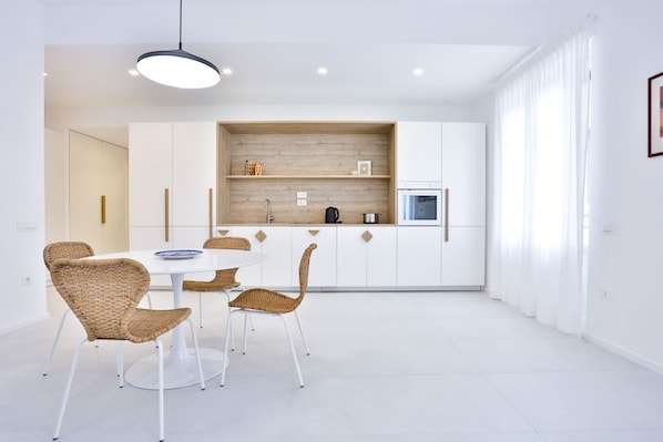 A modern kitchen with white cabinets, a built-in oven, and a dining area with wicker chairs and a white table.