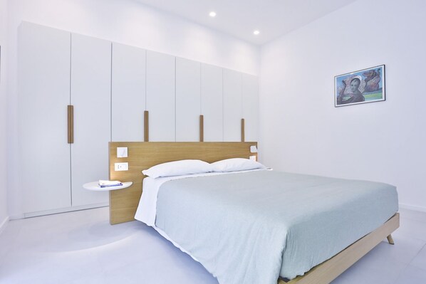 A modern bedroom with a wooden headboard, a single bedside table, and a wall-mounted artwork.