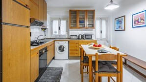 Una cocina compacta con armarios de madera, microondas, lavadora y comedor con mesa y sillas.