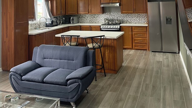 A modern kitchen with wooden cabinets, a stainless steel refrigerator, and a central island with seating. - Charming 1-bedroom 1 bath apt. in awesome D'Abadie with AC, WiFi, Washer/Dryer. (D'Abadie)