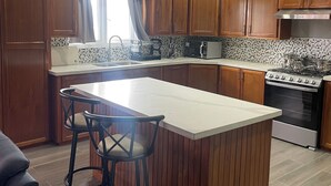 A modern kitchen with wooden cabinets, a large island with bar stools, a built-in oven, and a tiled backsplash. - Charming 1-bedroom 1 bath apt. in awesome D'Abadie with AC, WiFi, Washer/Dryer. (D'Abadie)